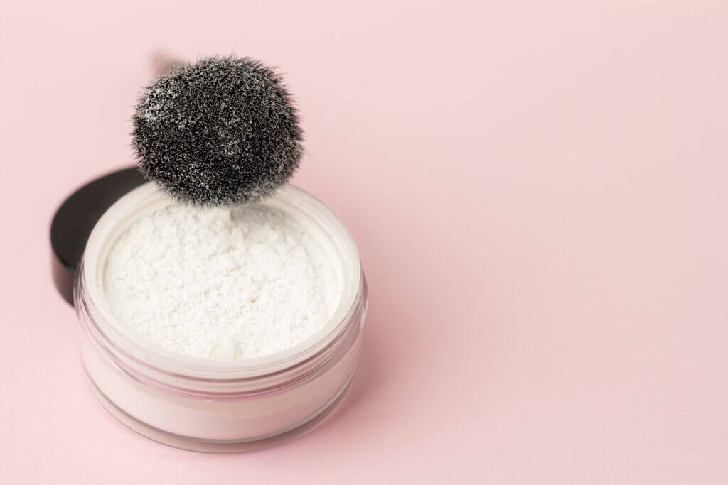 Loose white face powder with black brush.