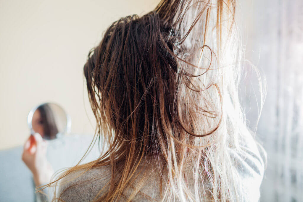 Close up of woman touching dirty, oily and greasy hair looking in mirror