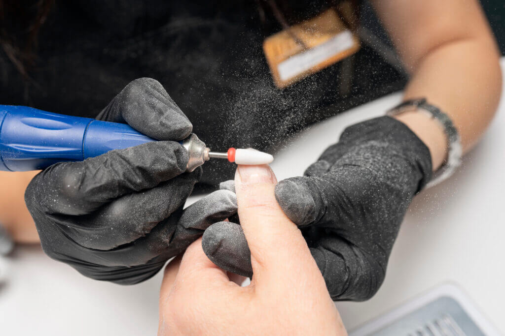 Manicurist is using a electric nail file drill in beauty salon