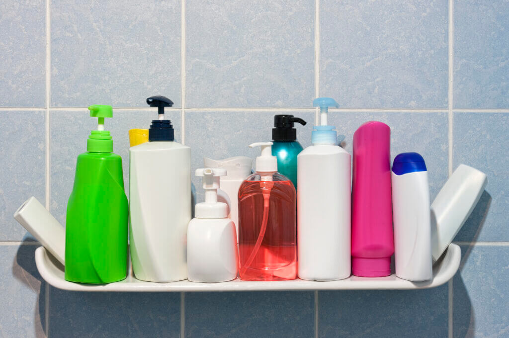 Many shampoo and soap bottles on a bathroom or shower shelf.