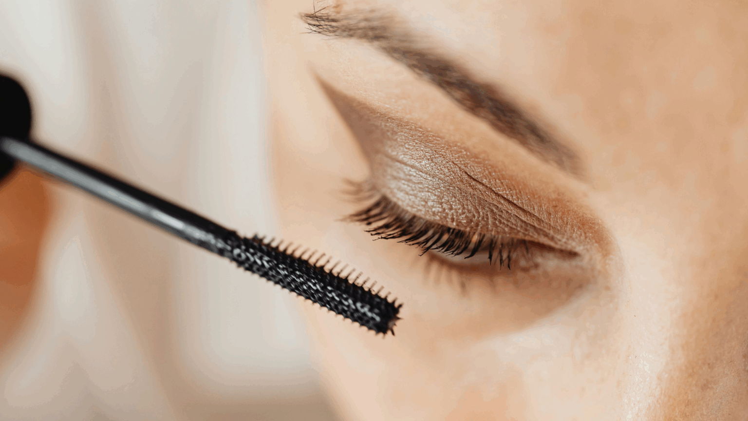 Woman applying mascara in a softly lit room