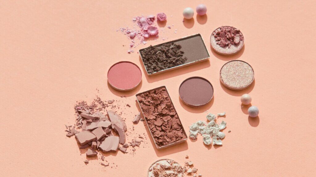 Crushed and whole makeup powders scattered on a pink surface