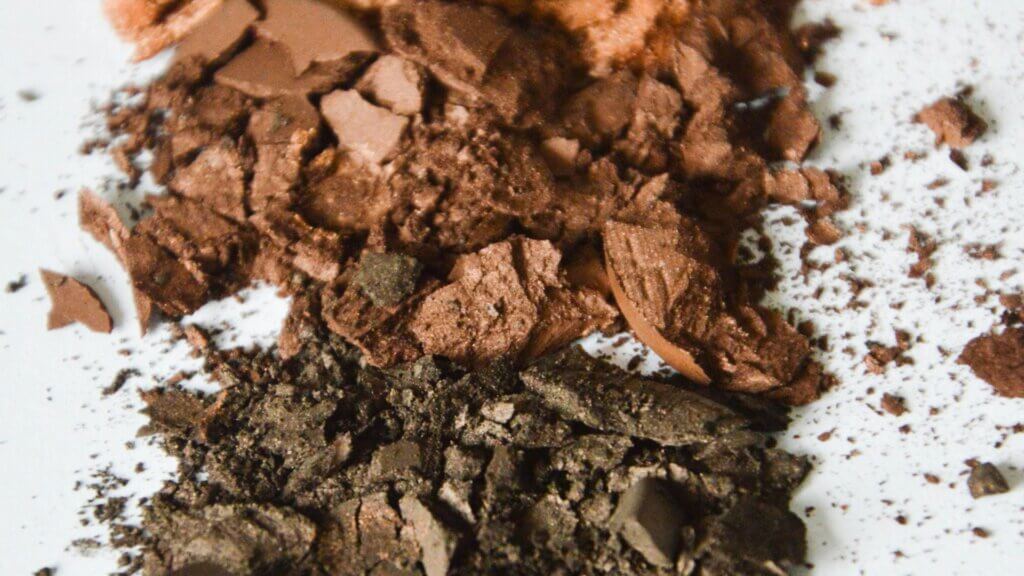 Crushed makeup powders in earthy tones on a soft surface