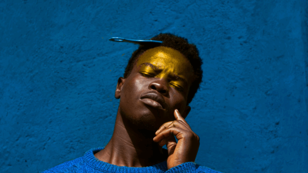 Man in a blue knit sweater standing against a blue wall with a decorative comb visible in hair