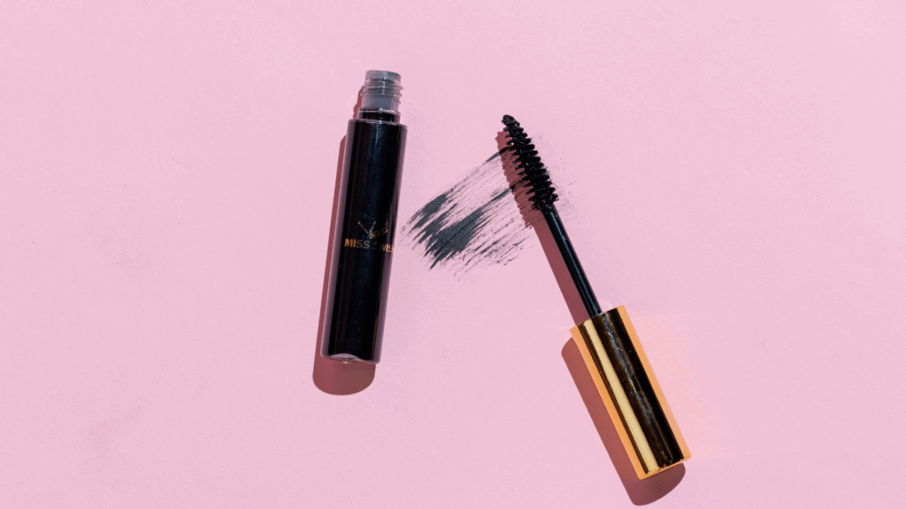 Silver and black mascara tube next to a brush on white surface