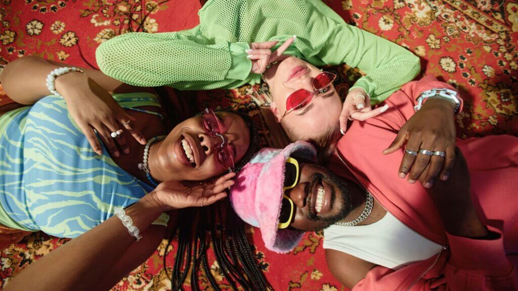 Top view closeup of three trendy young people lying on ornate carpet and smiling at camera