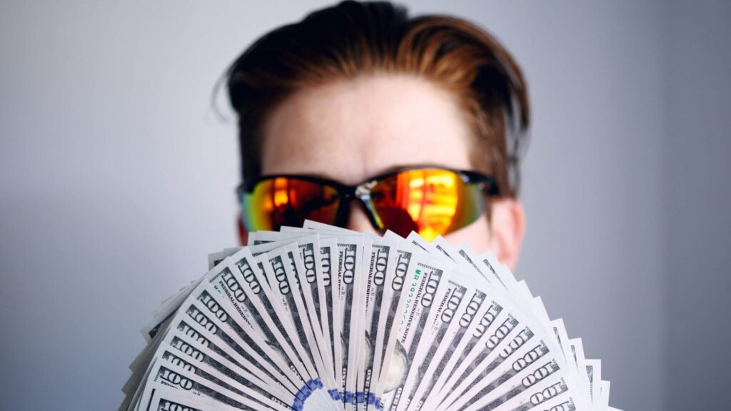 Person wearing black sunglasses holding a fan of US cash