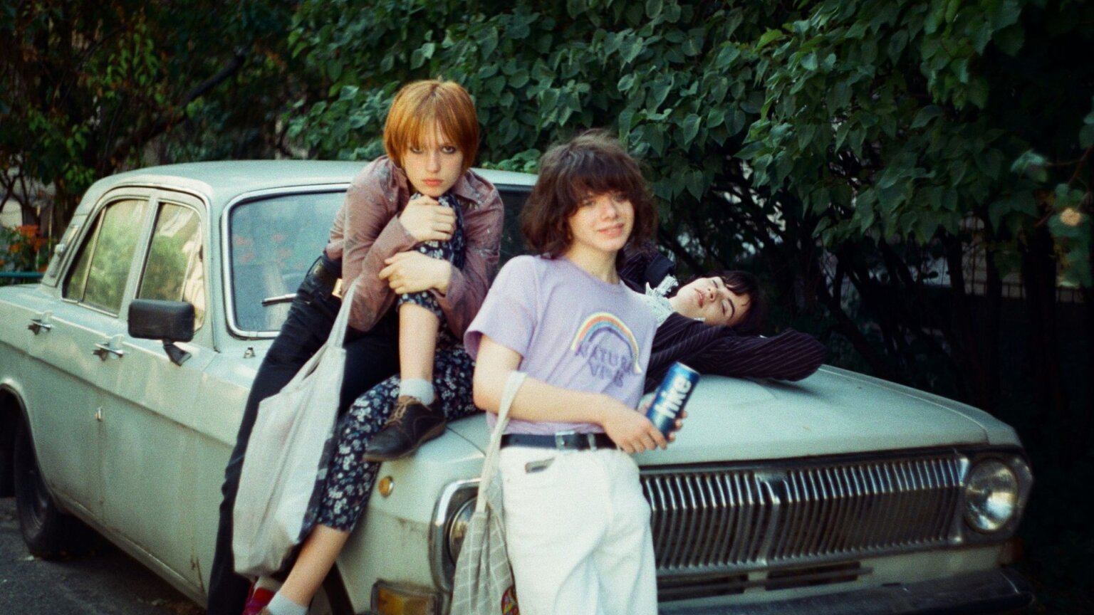Three young people leaning up against a car