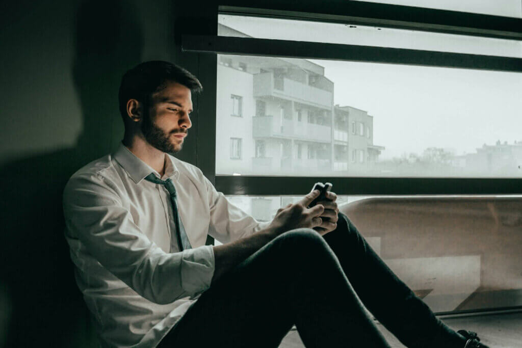 A man sitting against a wall looking at his phone