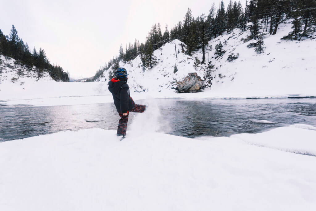 A boy kicking snow along a river
