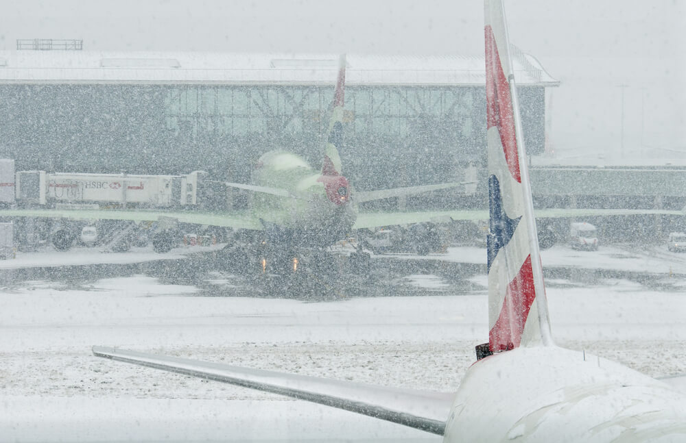 Airplane parked at a snow-covered airport gate during a blizzard as heavy snow falls on the tarmac.