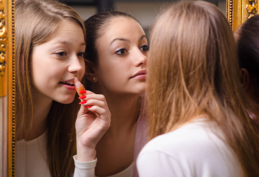 Teen girls putting makeup in front of the mirror