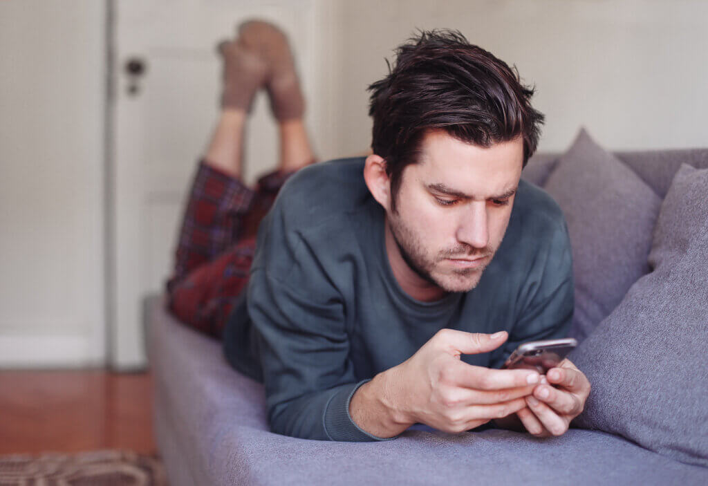 Man looking at his mobile phone while lying on a sofa