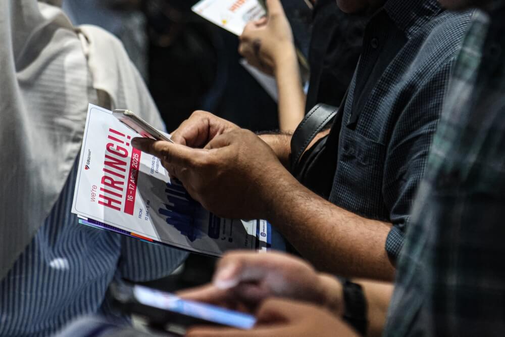 Job seeker holding a "We're hiring" company flyer in a job fair