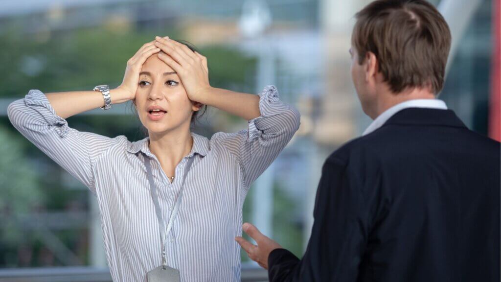 Woman holding her head in frustration while talking to a man in business attire outdoors.
