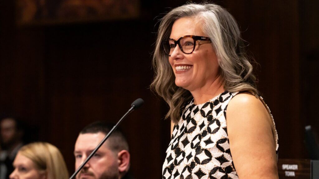 Gov. Hobbs smiling while speaking at a podium in a formal setting.