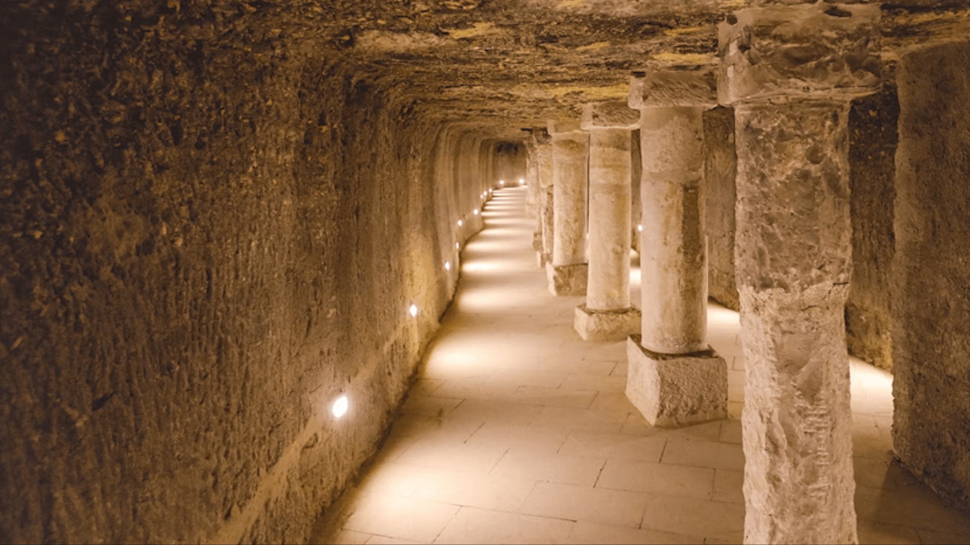 Long stone hallway with columns and lights inside an ancient underground structure.
