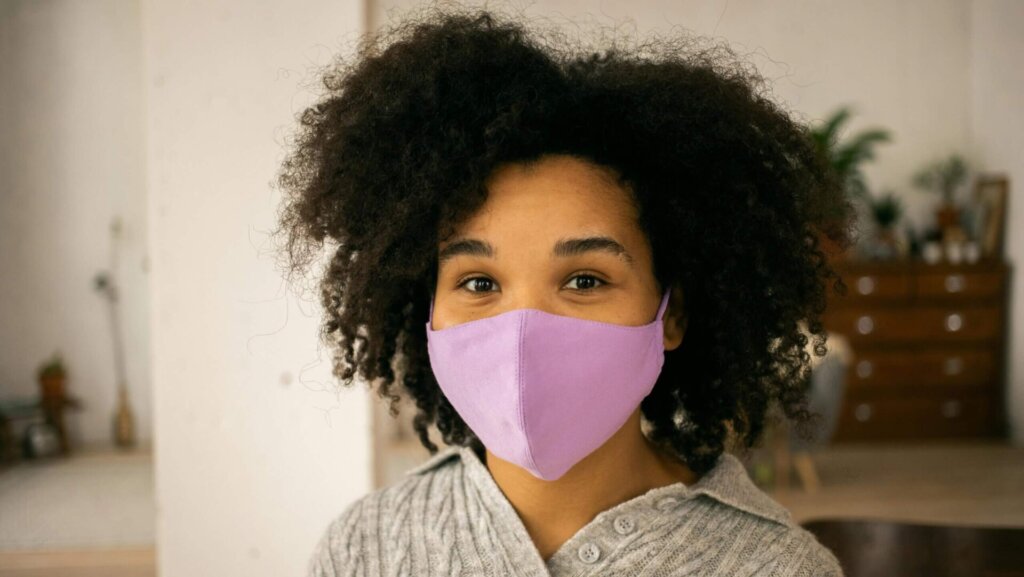 Black woman wearing a protective face mask, looking forward with a neutral expression.