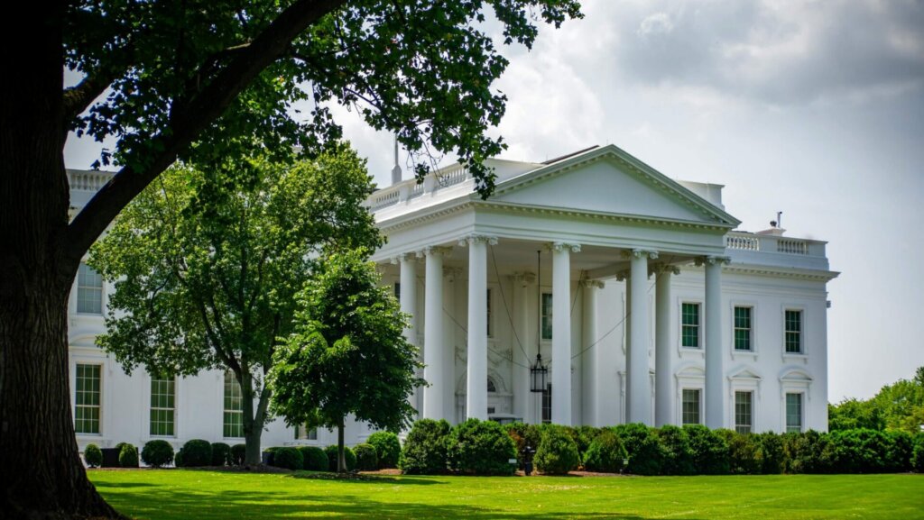 Exterior view of the White House surrounded by green trees on a clear day.