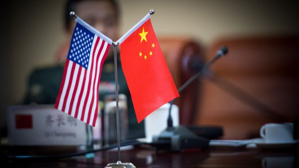 Small tabletop flags of the United States and China crossed on a stand, placed on a conference table during a formal diplomatic meeting.