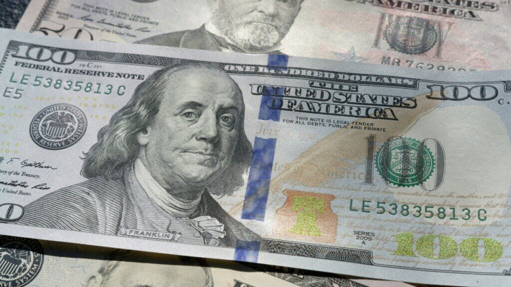 Modern blue $100 bill with security ribbon visible across the front