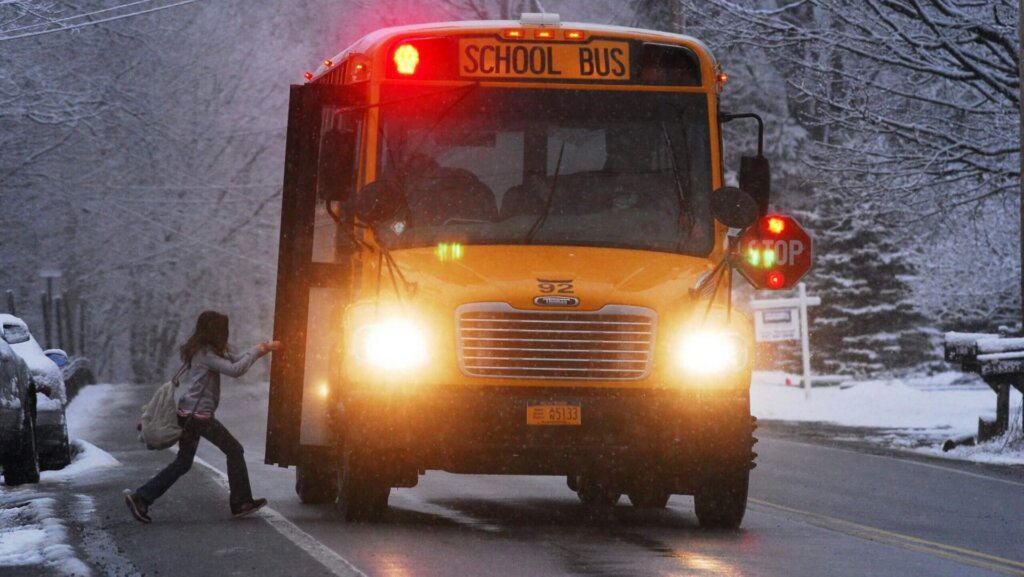 Snow-covered city street with parked cars and buildings during a winter day.