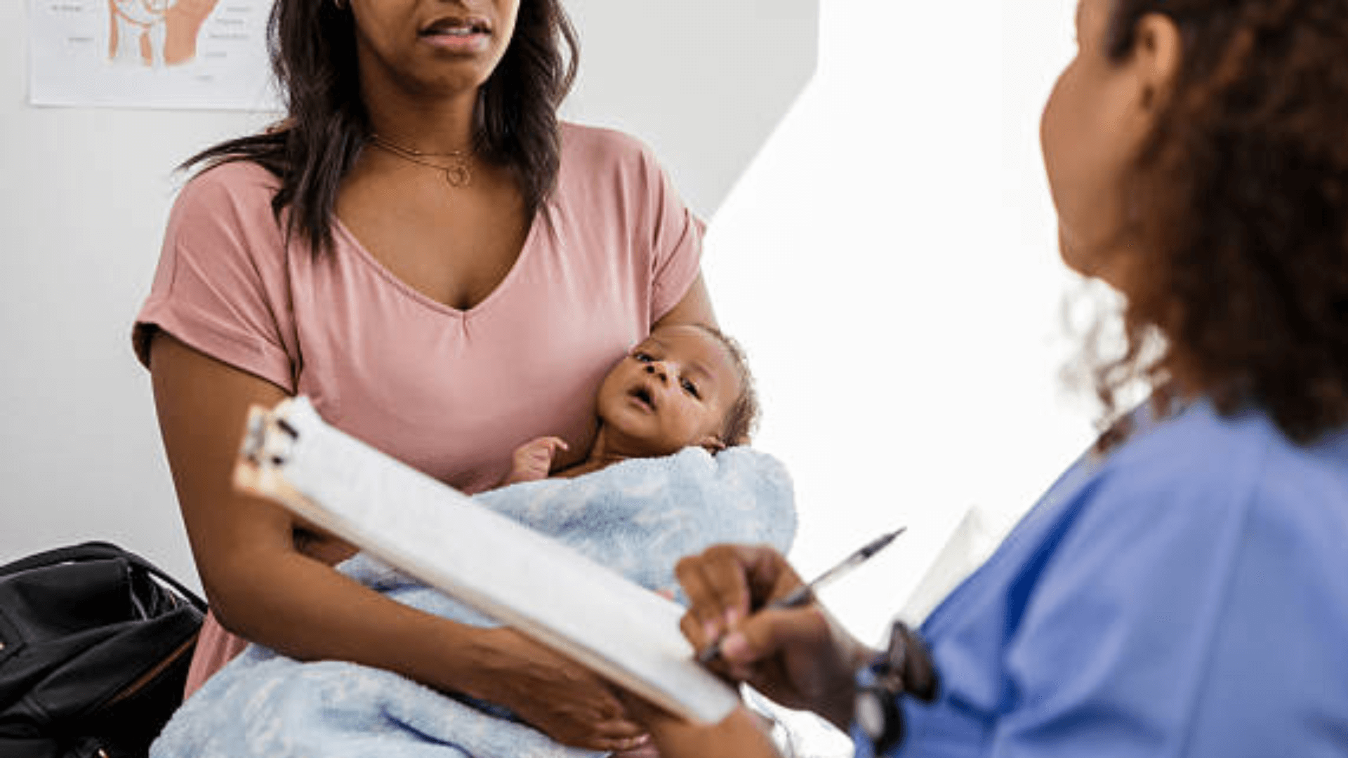 Mother holding baby while talking to a doctor with a clipboard.
