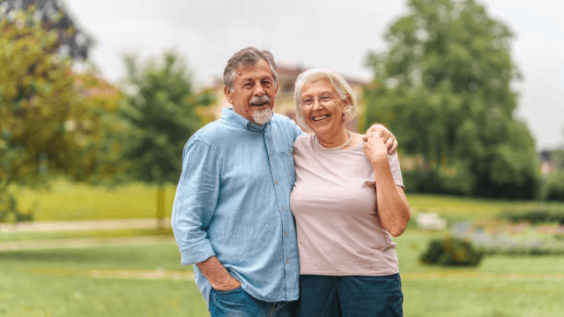 Happy senior couple standing close together in a park, smiling at the camera.