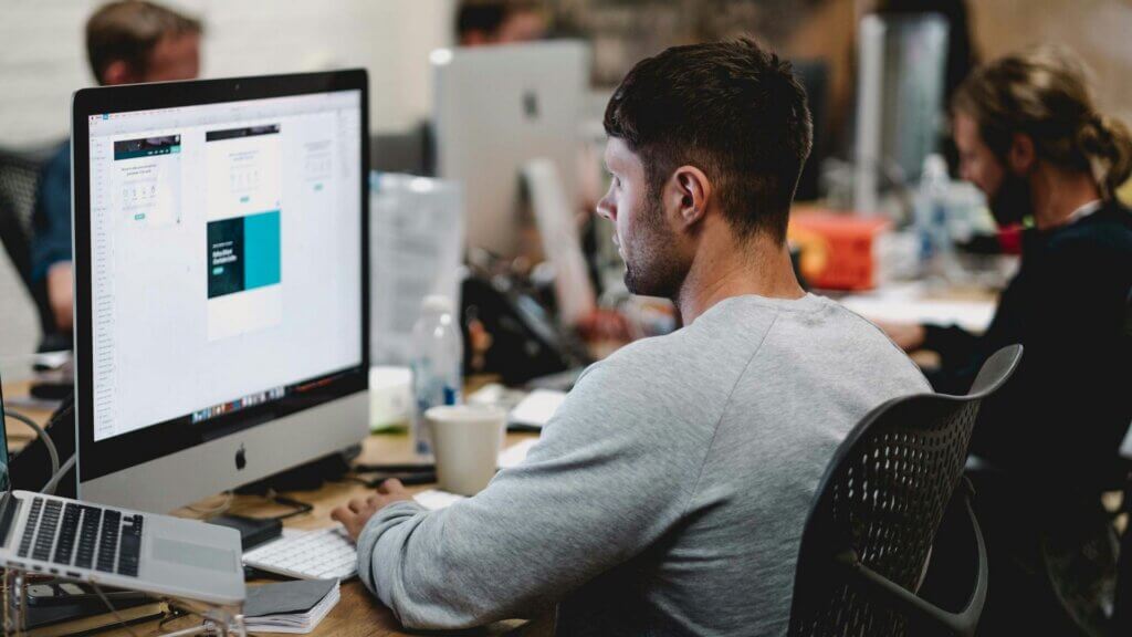 Man seated at a desk using an iMac computer in a home workspace