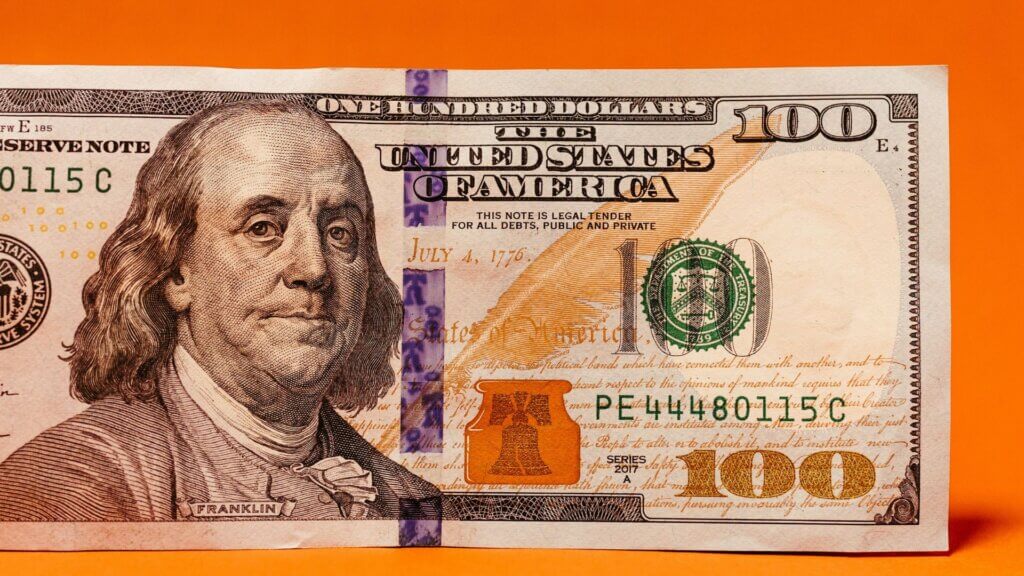 $100 bill placed on an orange background with high serial digits visible