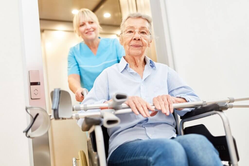 Senior stroke patient in a wheelchair being wheeled by a nurse