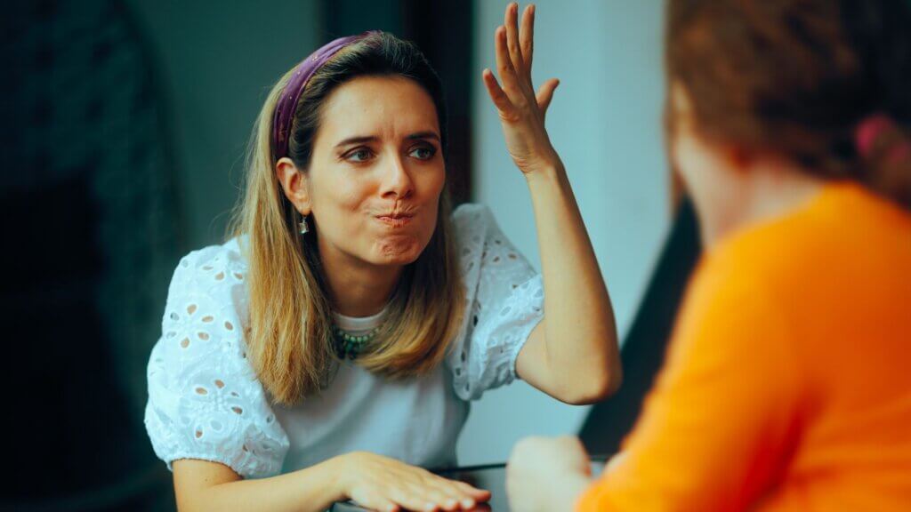 A woman speaking to another woman looking annoyed