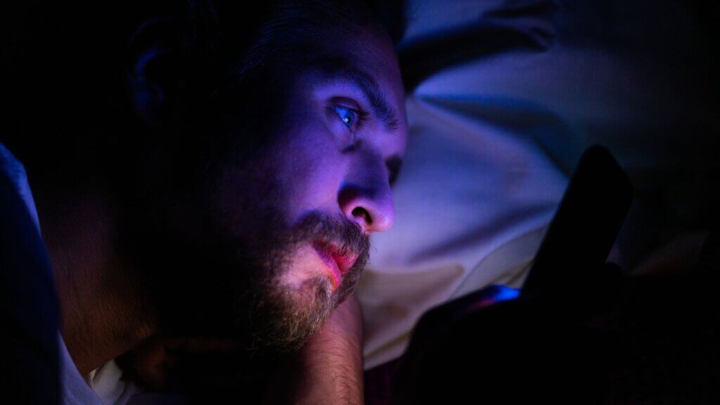 A man laying in bed staring at his phone