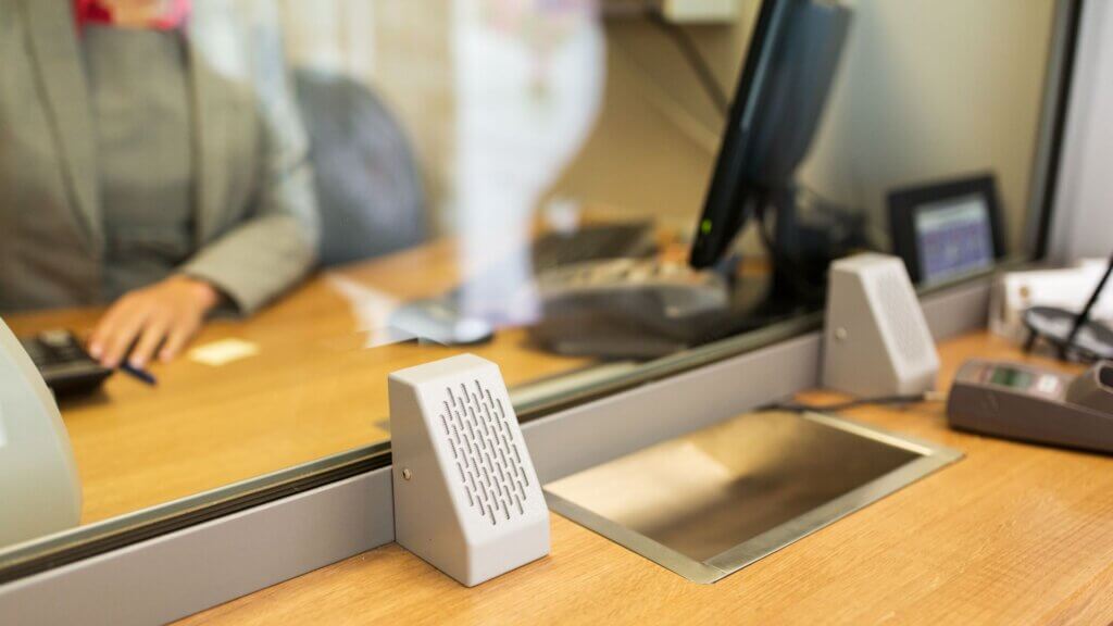 A bank teller area with a glass partition, microphone, and slide-through slot