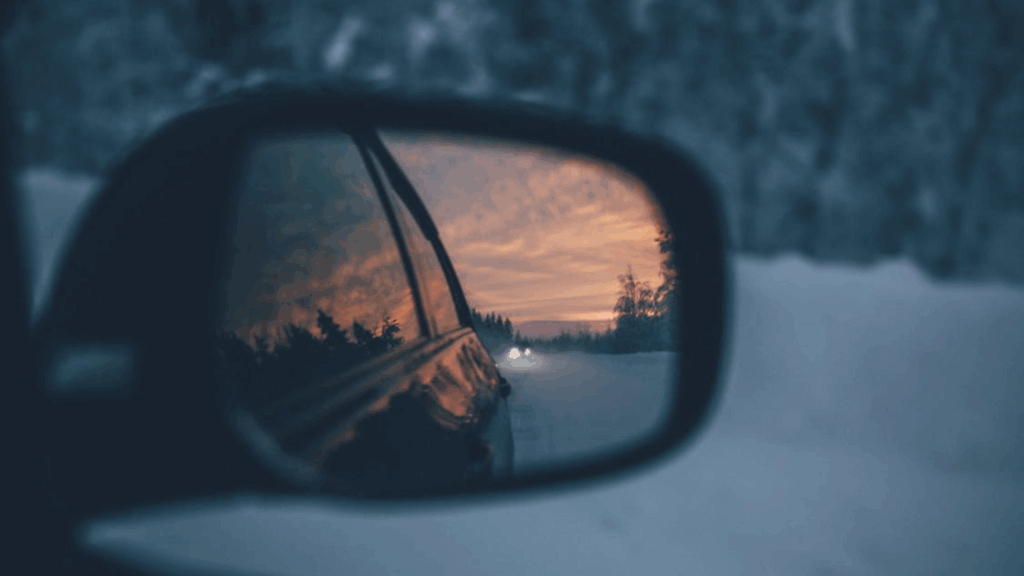 Side mirror view of a snowy road