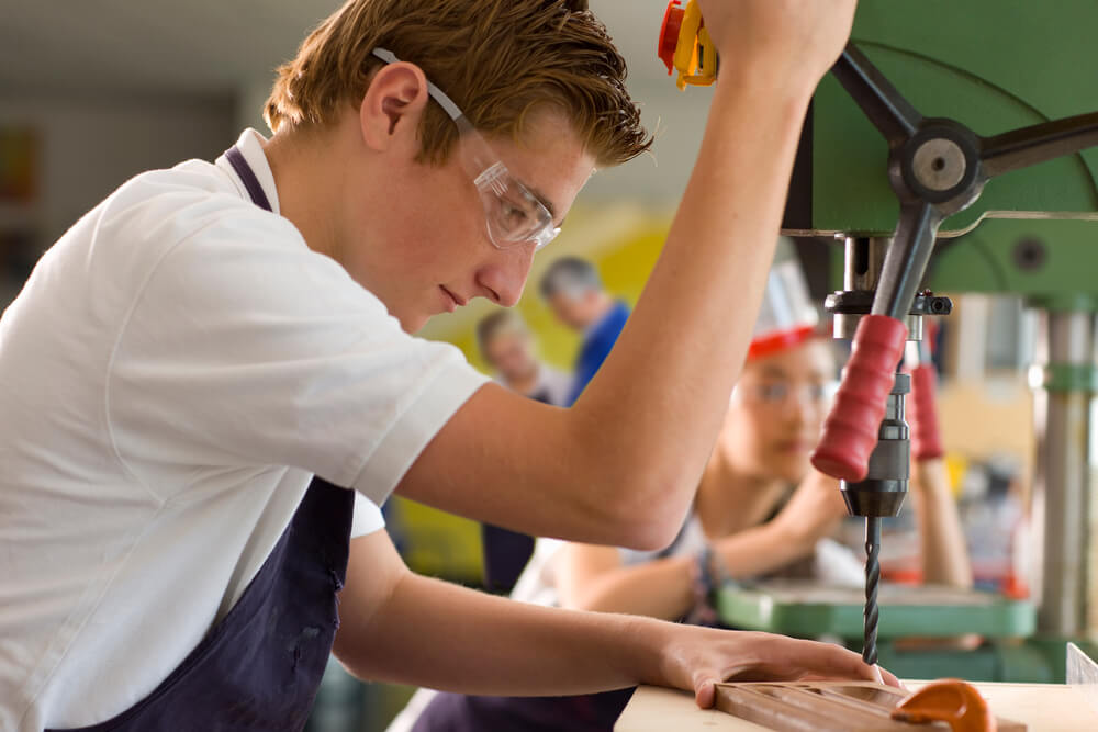 Student wearing safety glasses while using the drill machine in a vocational school