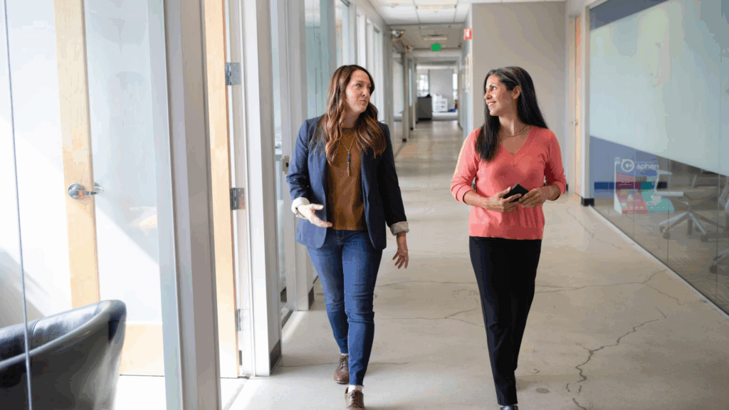 two women talking while walking in an office