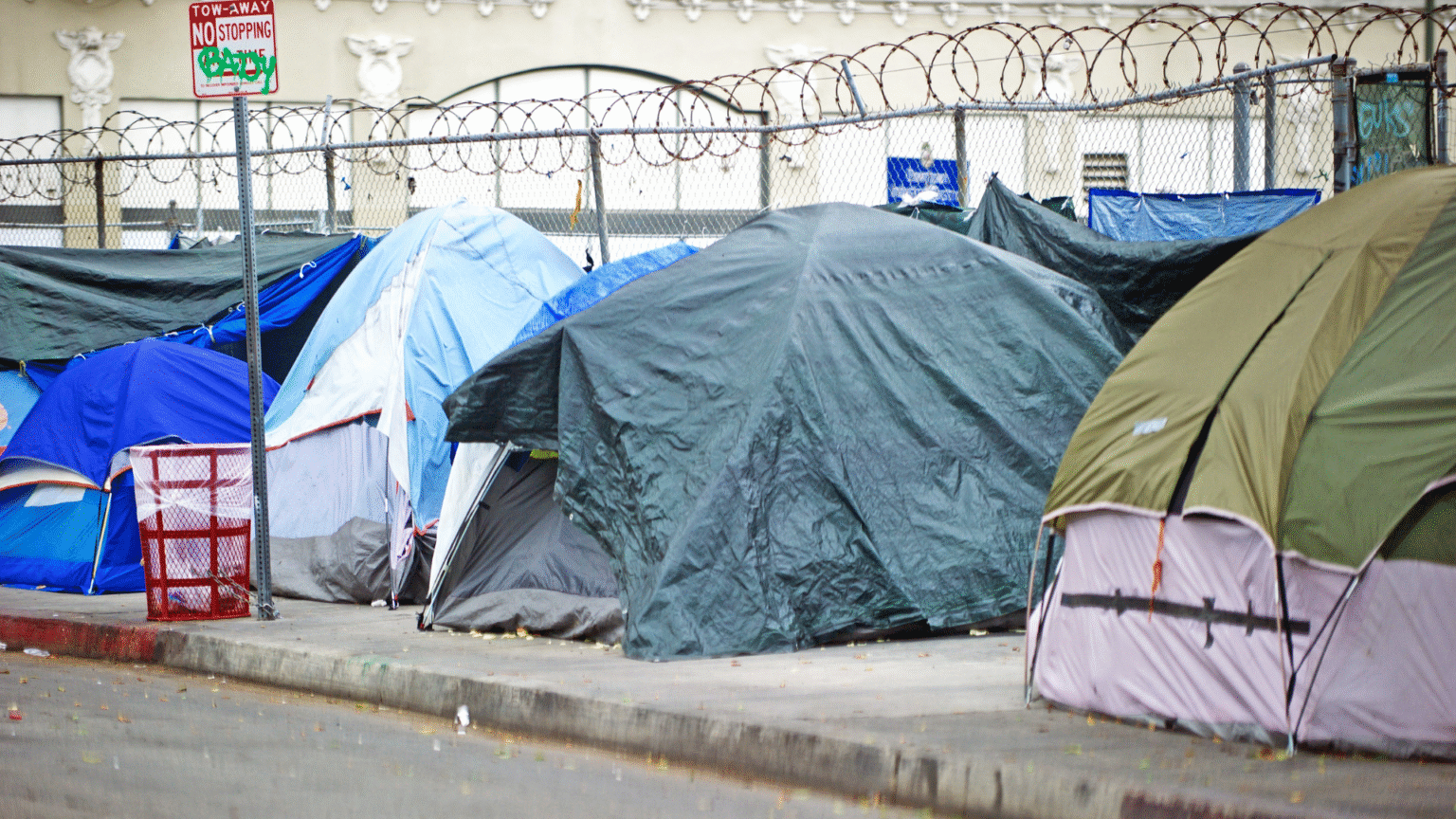 Row of tents on a city sidewalk showing a homeless encampment.