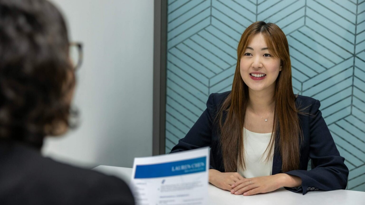 A woman in a business suit smiles during a job interview in a modern office environment