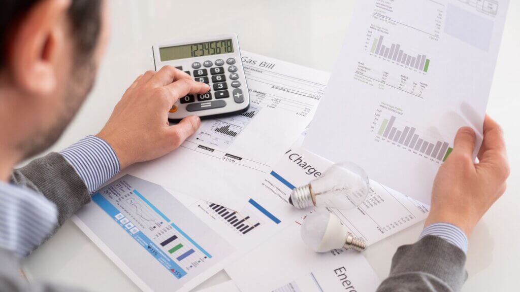 Person reviewing electricity bill papers with calculator on desk.