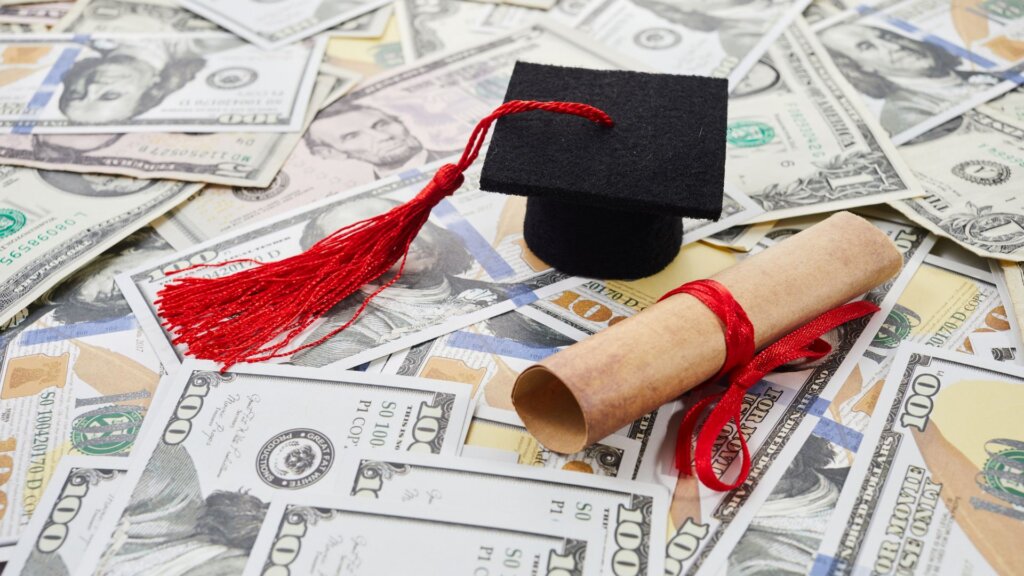 Miniature graduation cap resting on top of U.S. dollar bills.