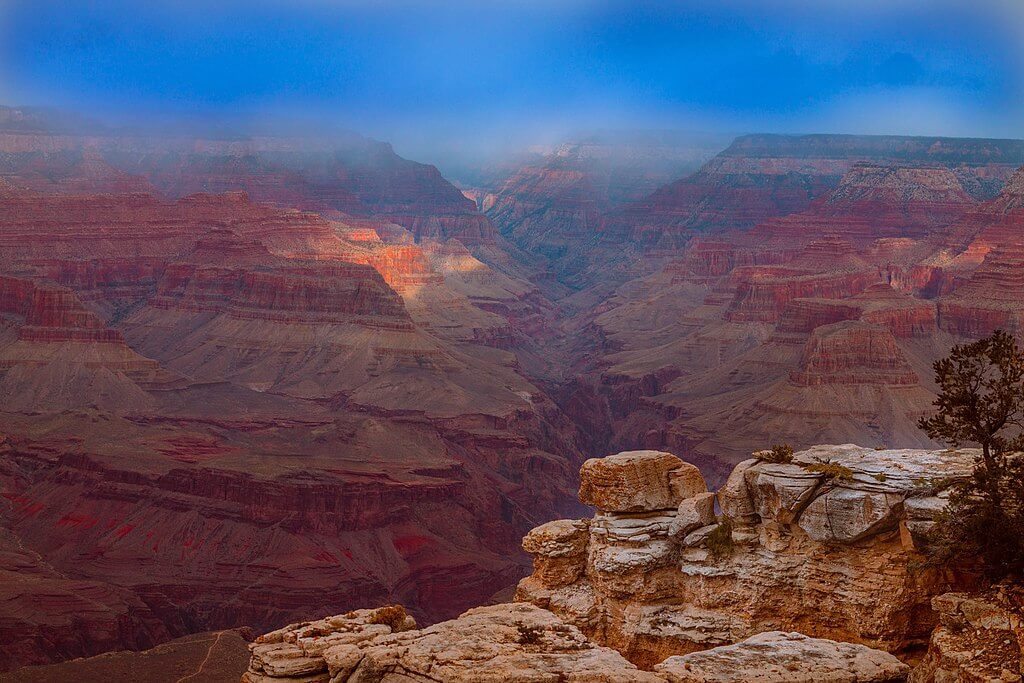 View of the Grand Canyon taken from near the El Tovar restaurant, showing layered red rock formations and a deep canyon under a hazy sky.