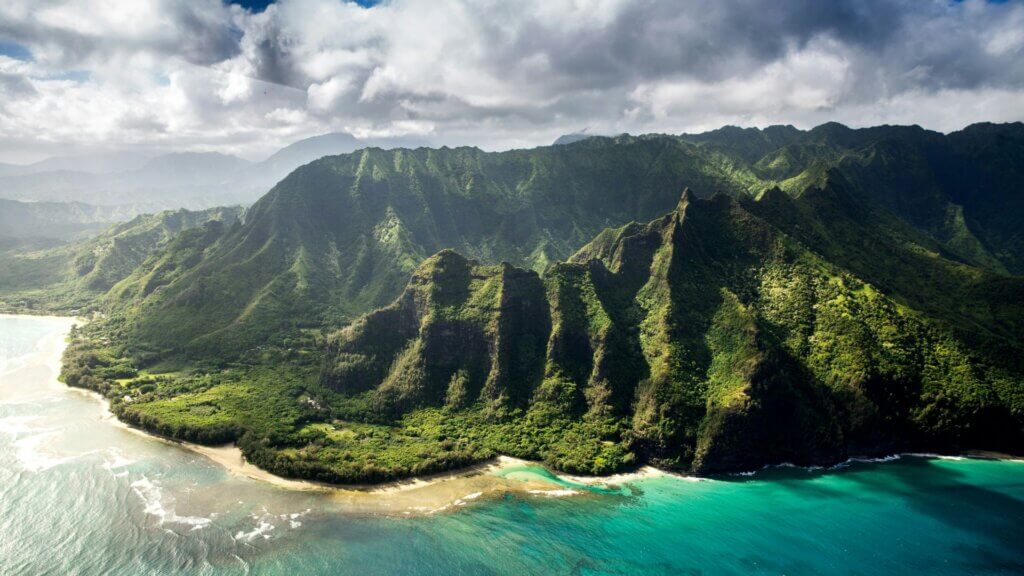 Aerial view of a green mountain beside a body of water under cloudy skies