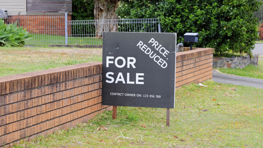 A “For Sale” sign in front of a house with a note that the price has been reduced.