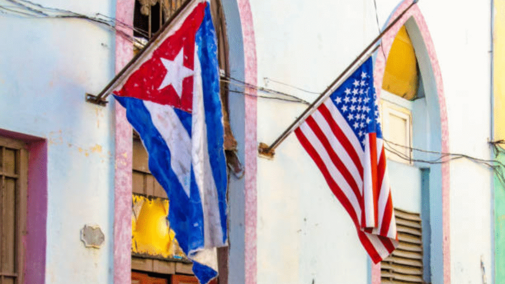 Cuban and United States flags hanging from a pastel-colored building facade.