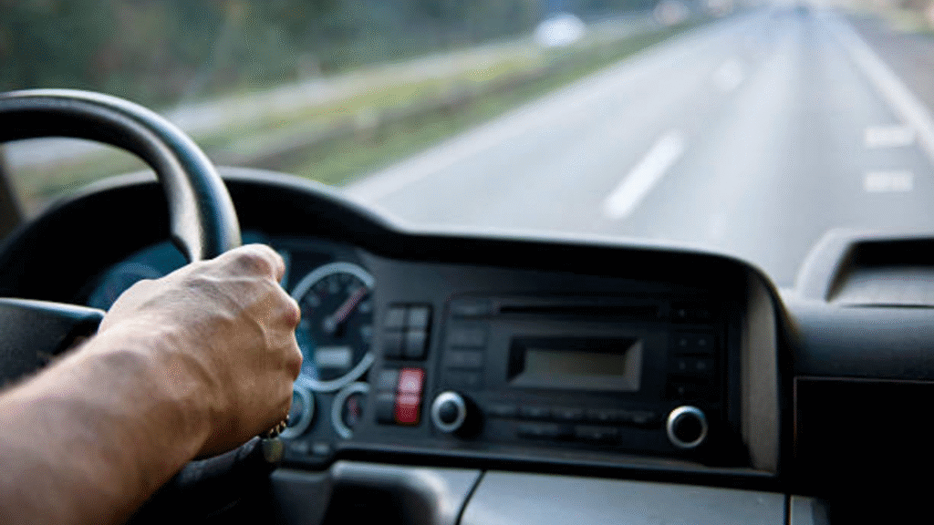 Driver holding a steering wheel while driving on a highway.