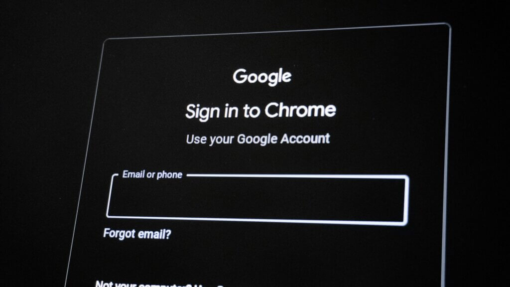 Close up of a Google sign in to Chrome screen showing fields for email or phone and a forgot email link against a dark background.