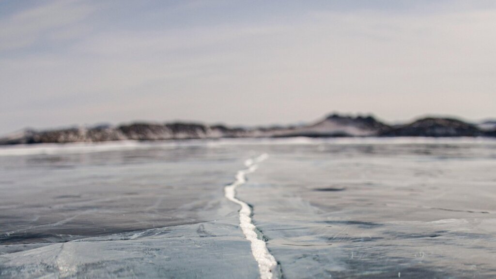 Snow-covered frozen lake stretching toward distant trees under a pale winter sky.