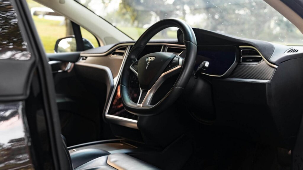 Interior view of a Tesla Model X showing dashboard and seats with a park setting outside the windows.