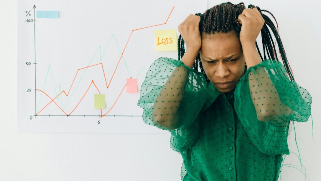 A woman wearing a green and white polka dot shirt covering her face with her hands, expressing stress or emotional distress.